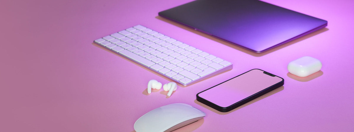 Teclado, mouse, celular, tablet y audífonos sobre fondo rosado